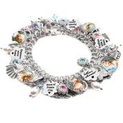 Silver charm bracelet inspired by Marie Antoinette, featuring vintage portraits of the Queen of France under glass cabochons, engraved tags with sayings like "Queen of France 1744," "Elegance never fades," and "Fashion tells a story," accented with pink and blue crystals, white pearl dangles, and miniature charms including a fan, crown, shoe, and ornate carriage, all displayed on a white background.