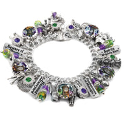 Handcrafted silver charm bracelet with a haunted graveyard theme, featuring spooky artwork under glass cabochons including tombstones, ghosts, haunted houses, and witches. Includes engraved tags with phrases like ‘Beware of Ghosts,’ ‘Zombies at Midnight,’ and ‘Spirits Welcome Here.’ Accented with green, purple, and orange Austrian crystals and Halloween-themed charms like skulls, cauldrons, and gravestones. Displayed on a white background.