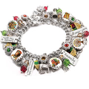 Handcrafted silver charm bracelet inspired by Kwanzaa, featuring charms with African art, women in traditional dress, seven candles (Mishumaa Saba), and engraved tags with words like ‘Umoja ~ Unity,’ ‘Kwanzaa,’ and ‘Zawadi ~ The Gift.’ Includes vibrant artwork under glass cabochons and charms in red, green, and gold. Embellished with Austrian crystals and cultural symbols. Displayed on a white background.