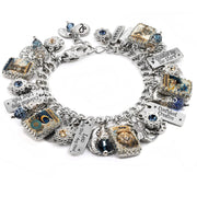Handcrafted silver charm bracelet inspired by the Leo zodiac sign, featuring celestial and astrological charms including a lion, stars, moons, and engraved tags. Includes vintage-style Leo artwork under glass cabochons, Leo birthdate charm, and sayings like ‘Confident Creative’ and ‘Guided by the Stars’. Embellished with blue and gold Austrian crystals. Displayed on a white background.