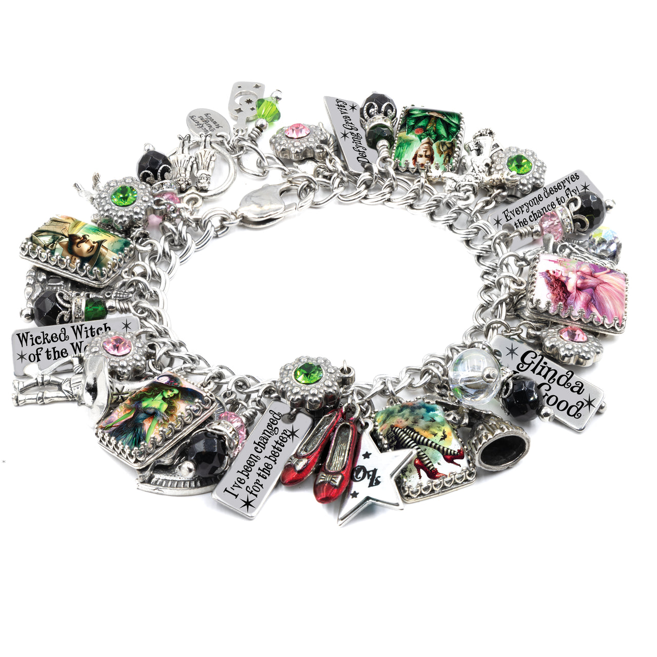 Handcrafted silver charm bracelet inspired by Wicked and The Wizard of Oz, featuring detailed charms of Elphaba, Glinda, ruby slippers, a tornado, and flying monkeys. Includes artwork under glass cabochons, engraved tags with sayings like ‘I’ve Been Changed for Good,’ ‘Wicked Witch of the West,’ and ‘Everyone Deserves the Chance to Fly.’ Embellished with pink, green, and black Austrian crystals. Displayed on a white background.