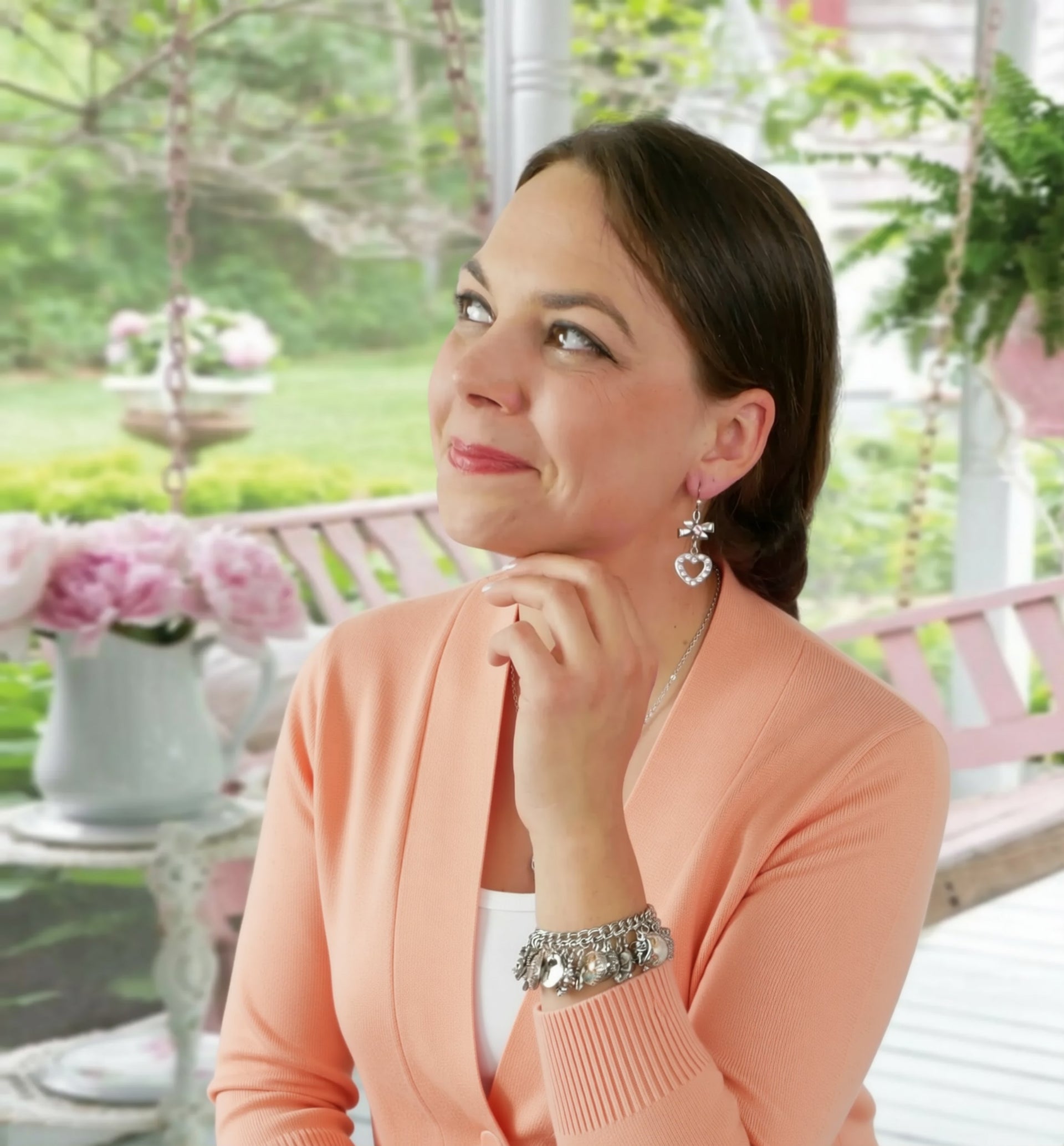 A woman in a peach sweater and a heart-shaped earring is sitting on a bench, looking off to the side with a thoughtful expression.