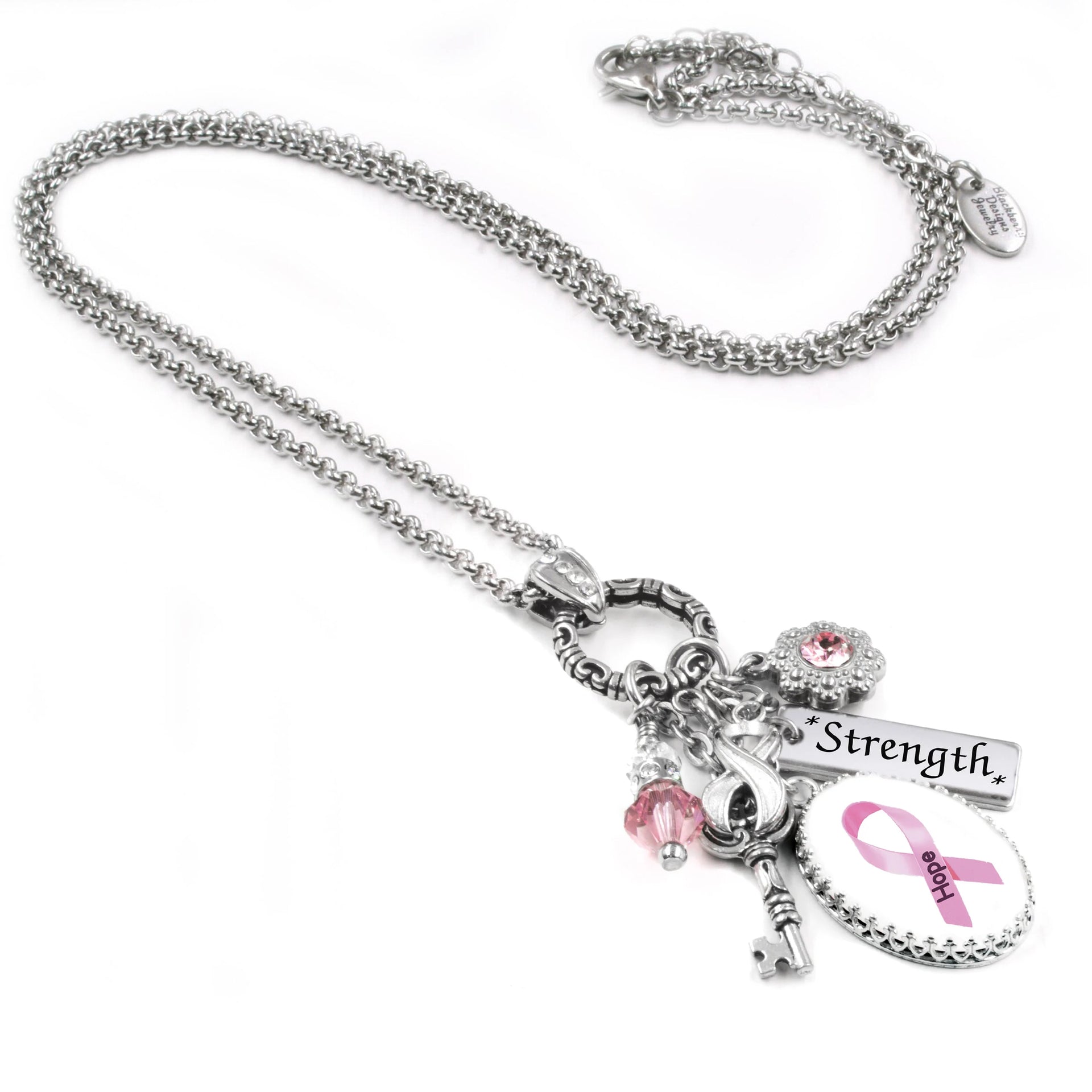 A silver necklace with various charms and pendants, including a pink ribbon charm, a key charm, and a "Strength" charm, as well as a small charm with the word "Love" on it.