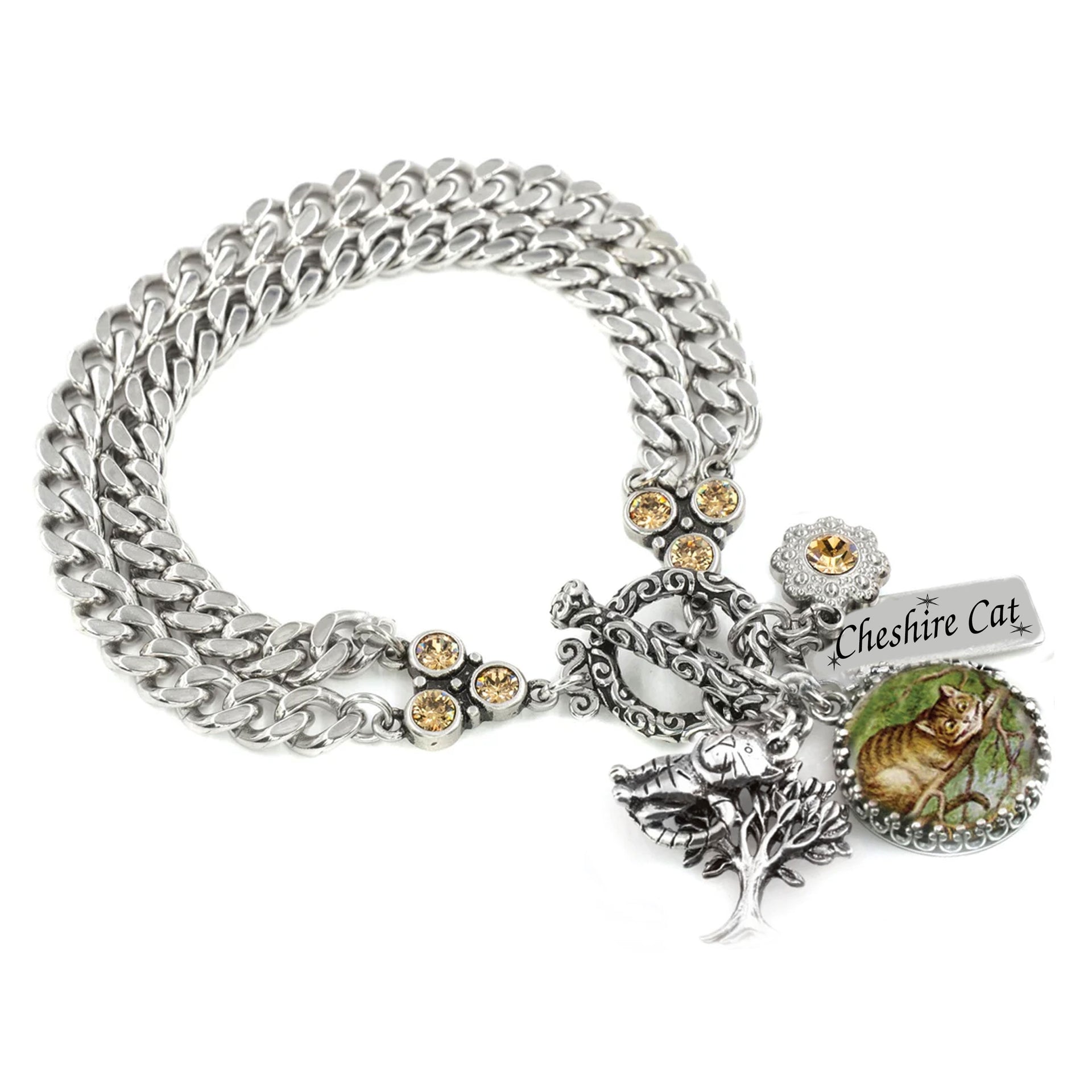 
Handcrafted Cheshire Cat charm bracelet from the Simply Collection featuring artist-designed double curb chain in 316L stainless steel with golden topaz crystal connector ends, ornate filigree toggle clasp, original John Tenniel Cheshire Cat illustration set under glass in scalloped silver cabochon setting, silver tree charm with bird, golden topaz crystal flower connector, and engraved Cheshire Cat bar charm. Handcrafted by artist Dea Shelton, Blackberry Designs Jewelry, California.