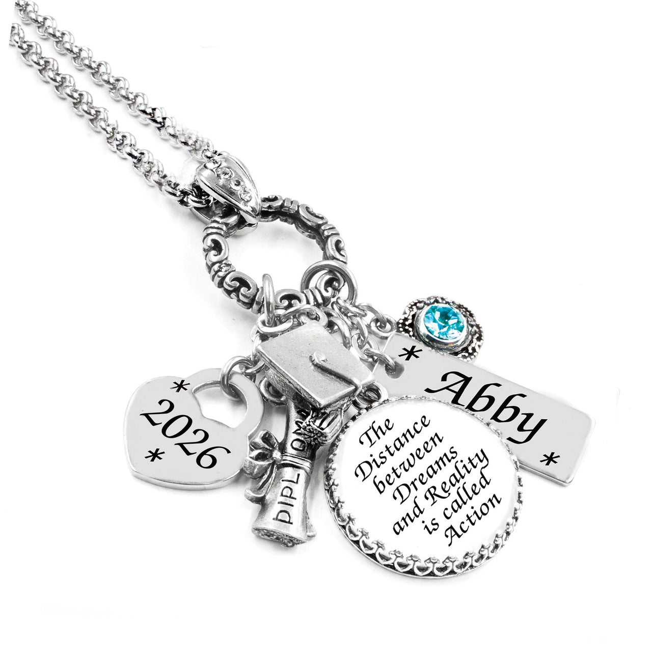 Silver necklace with multiple charms including a heart with '2026', a diploma, and a circular charm with text on a white background.
