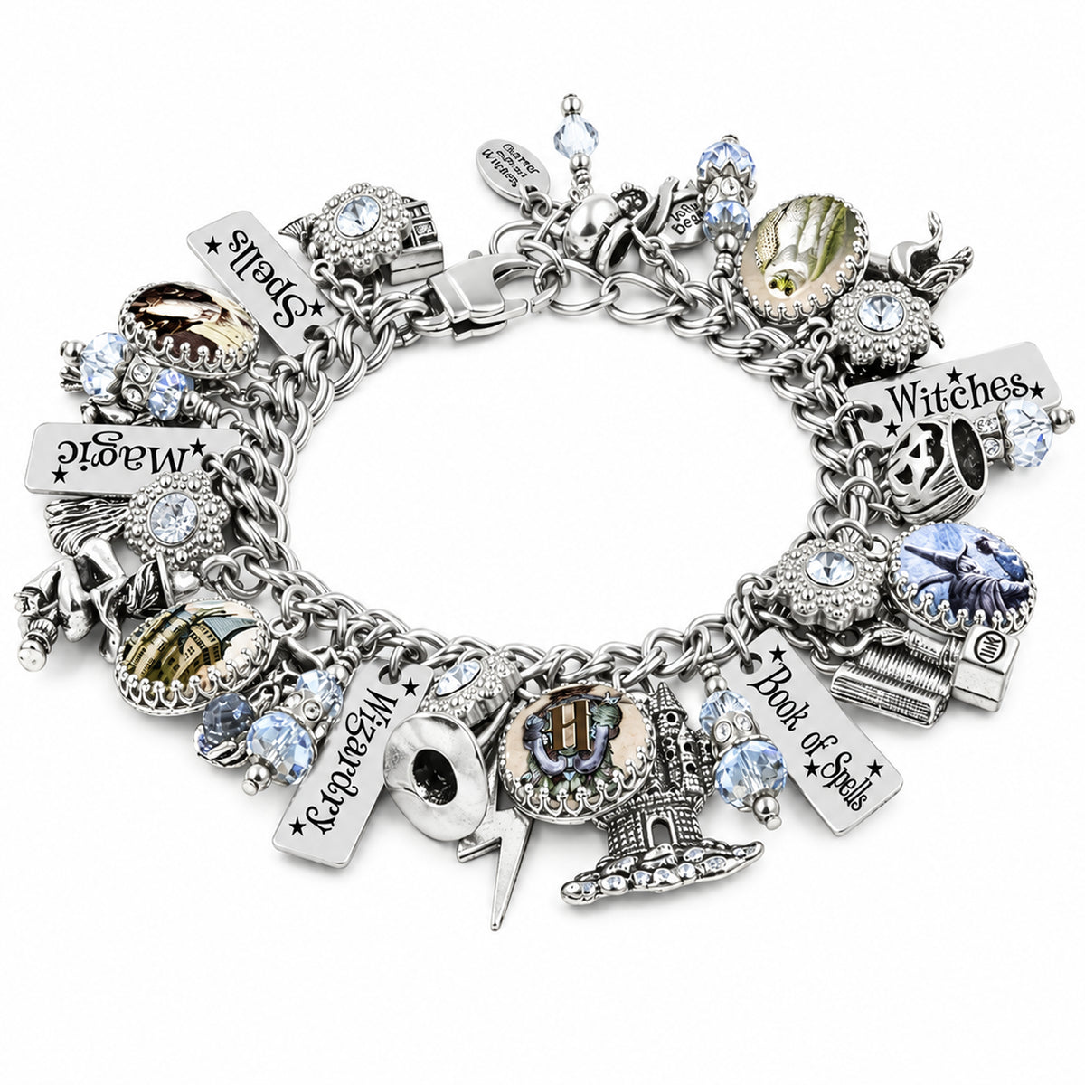 A silver charm bracelet featuring various gothic and witch-themed charms, including a cauldron, dagger, skull, and engraved tags reading 'Witches', 'Book of spells, magic and wizardy', embellished with clear rhinestones and light blue faceted crystals.