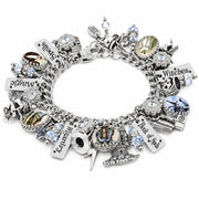 A silver charm bracelet featuring various gothic and witch-themed charms, including a cauldron, dagger, skull, and engraved tags reading 'Witches', 'Book of spells, magic and wizardy', embellished with clear rhinestones and light blue faceted crystals.