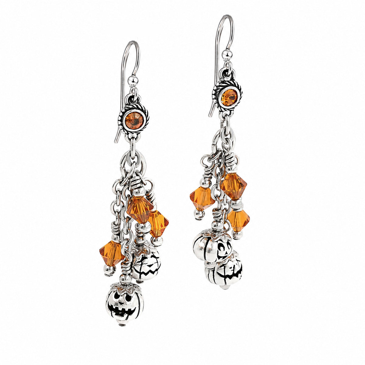 A pair of silver-toned dangle earrings with orange faceted crystal beads, small skull charms, and carved pumpkin charms on a plain white background.