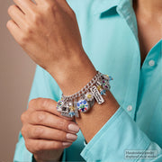 A close-up of a person wearing a silver charm bracelet with multiple colorful and personalized charms, including a small sign that reads 'L.A.