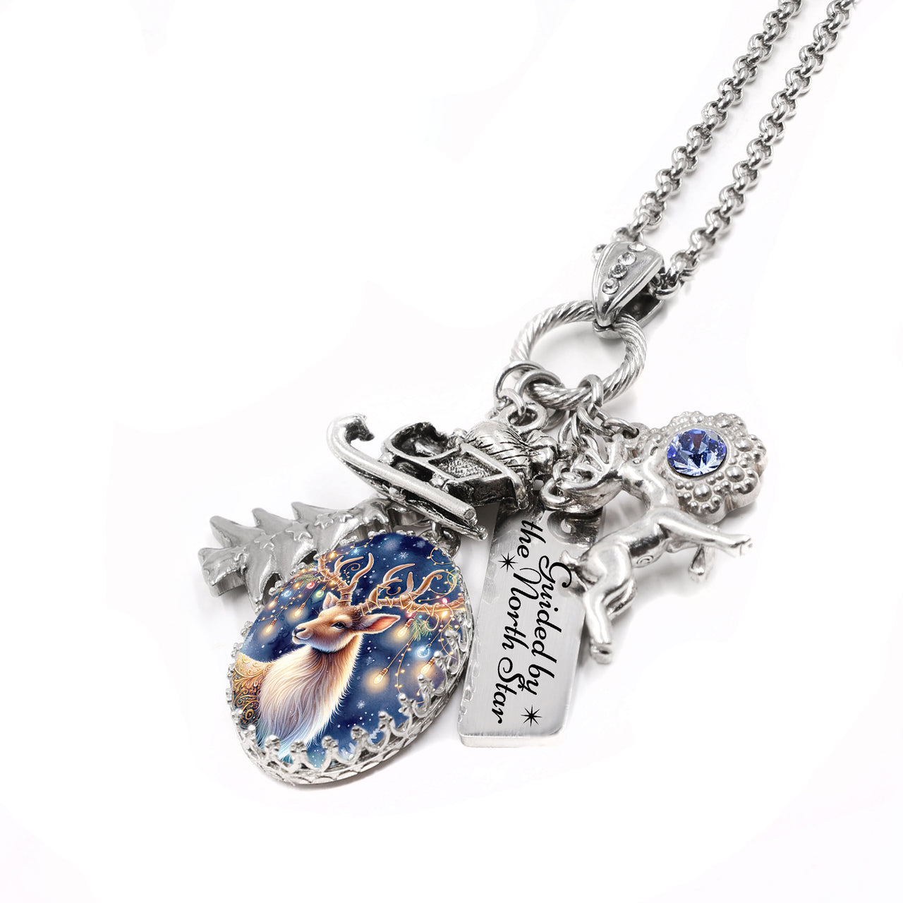 Silver reindeer charm necklace with sleigh, pine tree, and “Guided by the North Star” tag, blue crystal accent, on tarnish-free stainless chain.