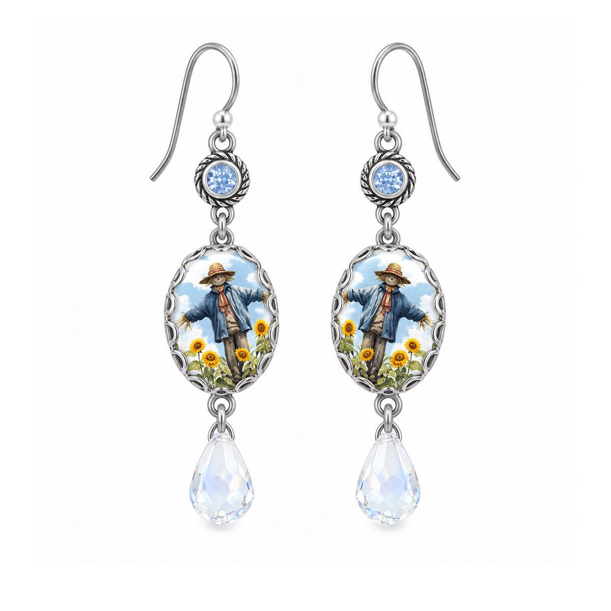 A pair of silver-toned dangle earrings featuring oval charms with an illustrated scarecrow in a blue coat and yellow flowers, with teardrop-shaped clear crystal drops below.