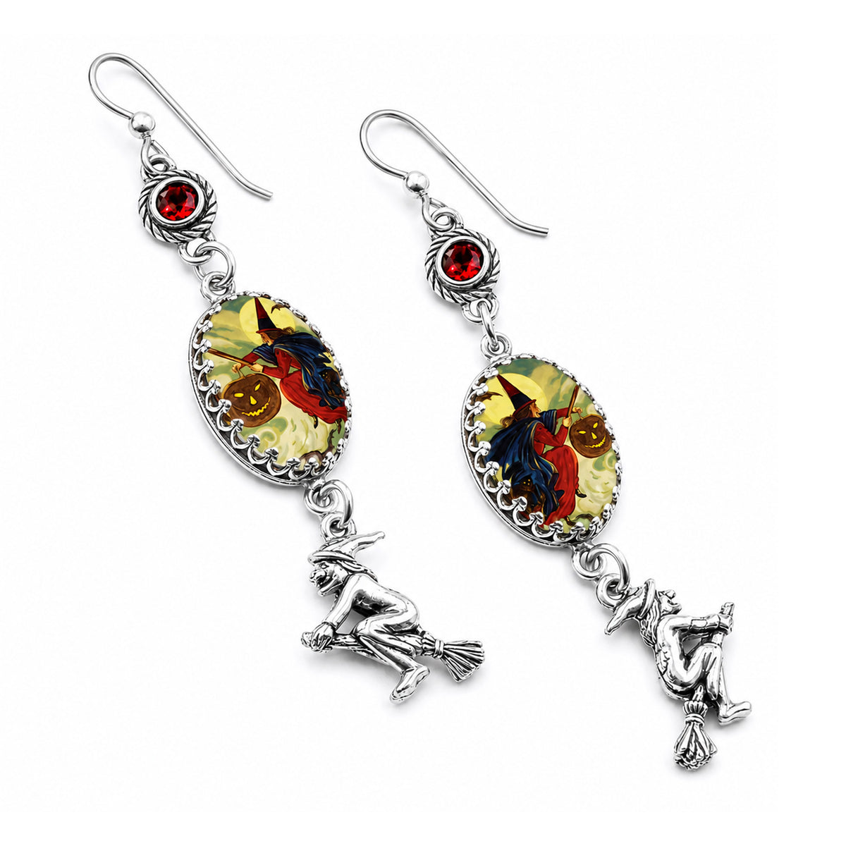 A pair of silver-toned dangle earrings with witch-themed charms. Each earring features a small red gemstone, an oval cabochon showing a witch riding a broomstick against a yellow and orange background, and a dangling silver witch figure on a broom.