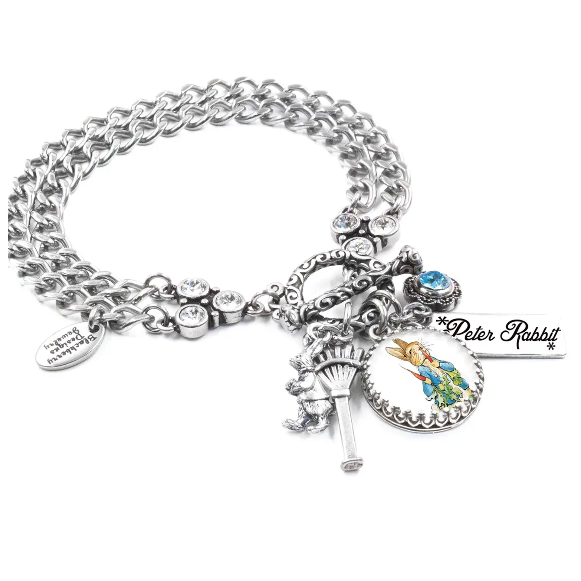 A silver-toned charm bracelet with various charms, including a key, a teddy bear, and a blue gemstone.