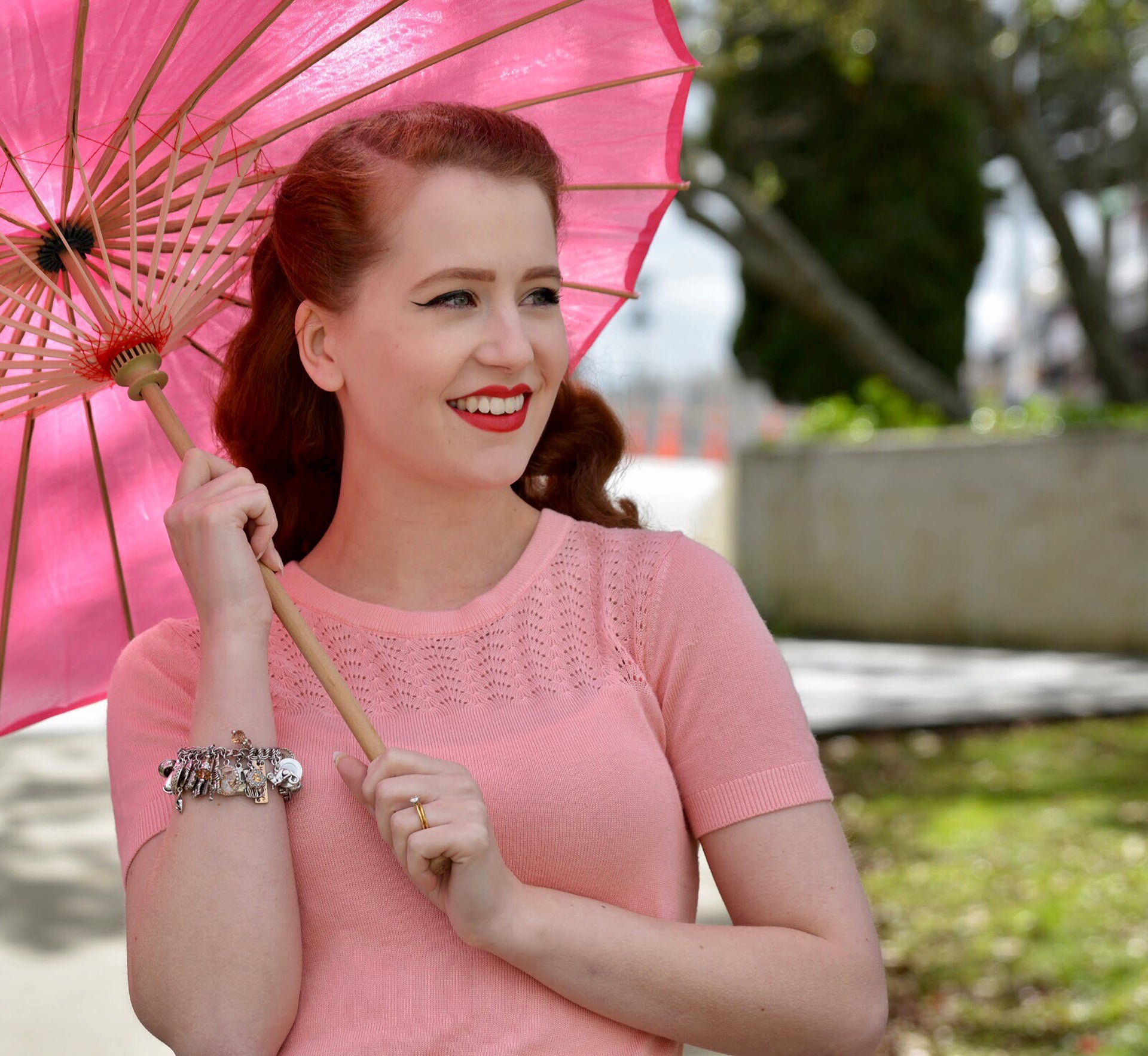 woman holding pink umbrella wearing cat charm bracelet